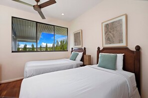 Ein Hotelzimmer mit zwei Betten, einem Deckenventilator, großen Fenstern mit Blick auf Bäume und gerahmten Kunstwerken an den Wänden.