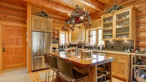 A wooden cabin interior with a central island, bar stools, a refrigerator, and a hanging light fixture. - 'Riverfront Ranch' Craig, Montana (Cascade)