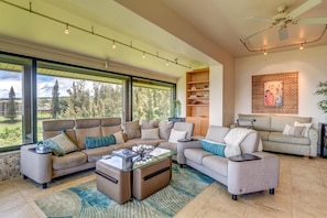 A spacious living room with a large sectional sofa, a glass coffee table, and a bookshelf. - Kapalua Ridge | Ocean View 5 BR, Sleeps 14 | Car Incl. w/ 6+ Nights | KRV ML-2165 by KBM (Lahaina)