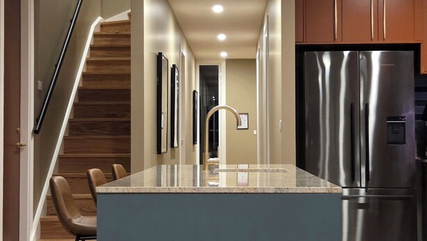 A modern kitchen with a central island, stainless steel appliances, and a wooden staircase. - Luxury accommodation Jindabyne. Weekly and monthly discounts (Jindabyne)