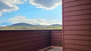 A balcony with a view of a green landscape and hills under a partly cloudy sky. - Luxury accommodation Jindabyne. Weekly and monthly discounts (Jindabyne)