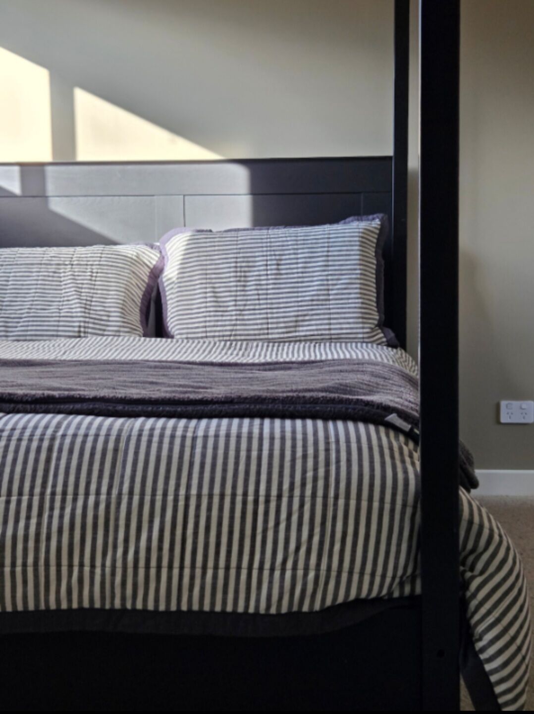 Een bed met gestreept beddengoed en een hoofdbord.