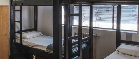 A bunk bed room with a ceiling fan, a window with blinds, and a wooden floor.