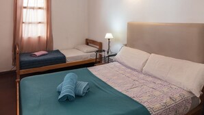 A hotel room with two beds, a bedside table with a lamp, and a window with curtains. - Hostel Pituco (Mendoza)