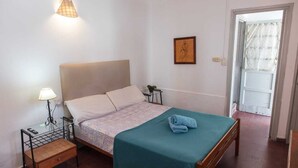 A neatly arranged bedroom with a bed, bedside lamps, a small table, and a door leading to another room. - Hostel Pituco (Mendoza)