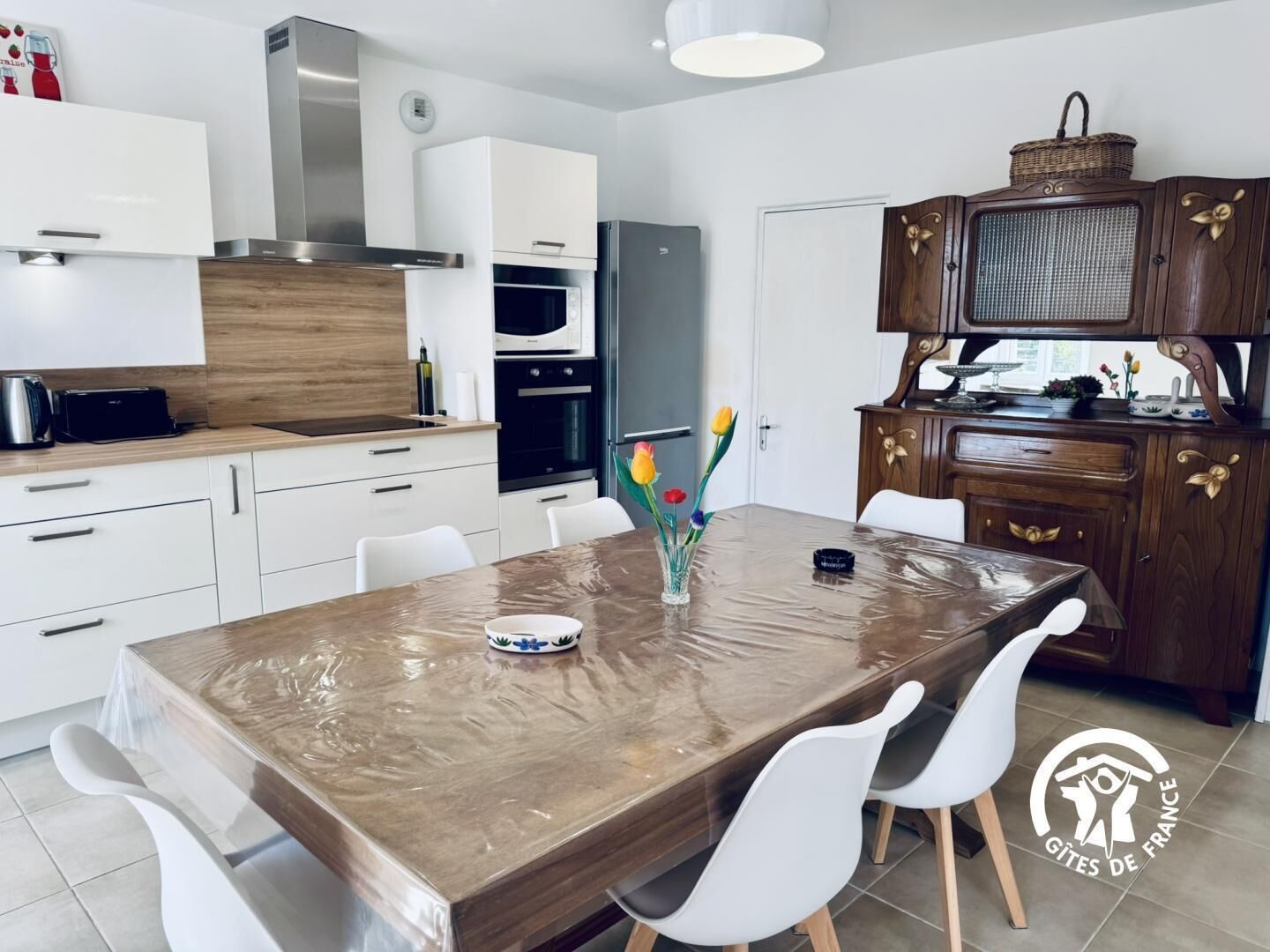 A modern kitchen with white cabinets, a wooden countertop, and a dining area with a marble table and white chairs.