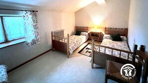 A room with two wooden beds, a window with floral curtains, a radiator, and a small table with a lamp. - La Migance - ALZONNE (ALZONNE)