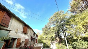 A narrow street with buildings on either side, a wooden gate, and a large tree in the foreground. - La Migance - ALZONNE (ALZONNE)