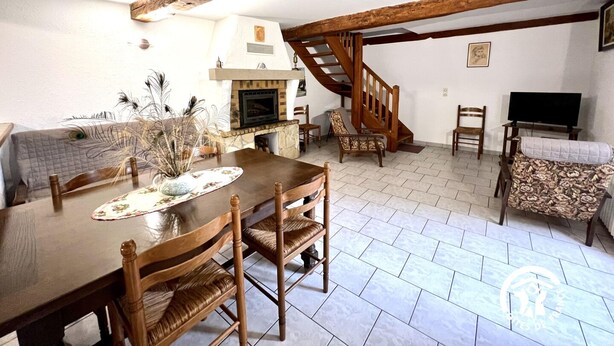 A spacious living room with a wooden dining table, chairs, a fireplace, and a staircase. - La Migance - ALZONNE (ALZONNE)