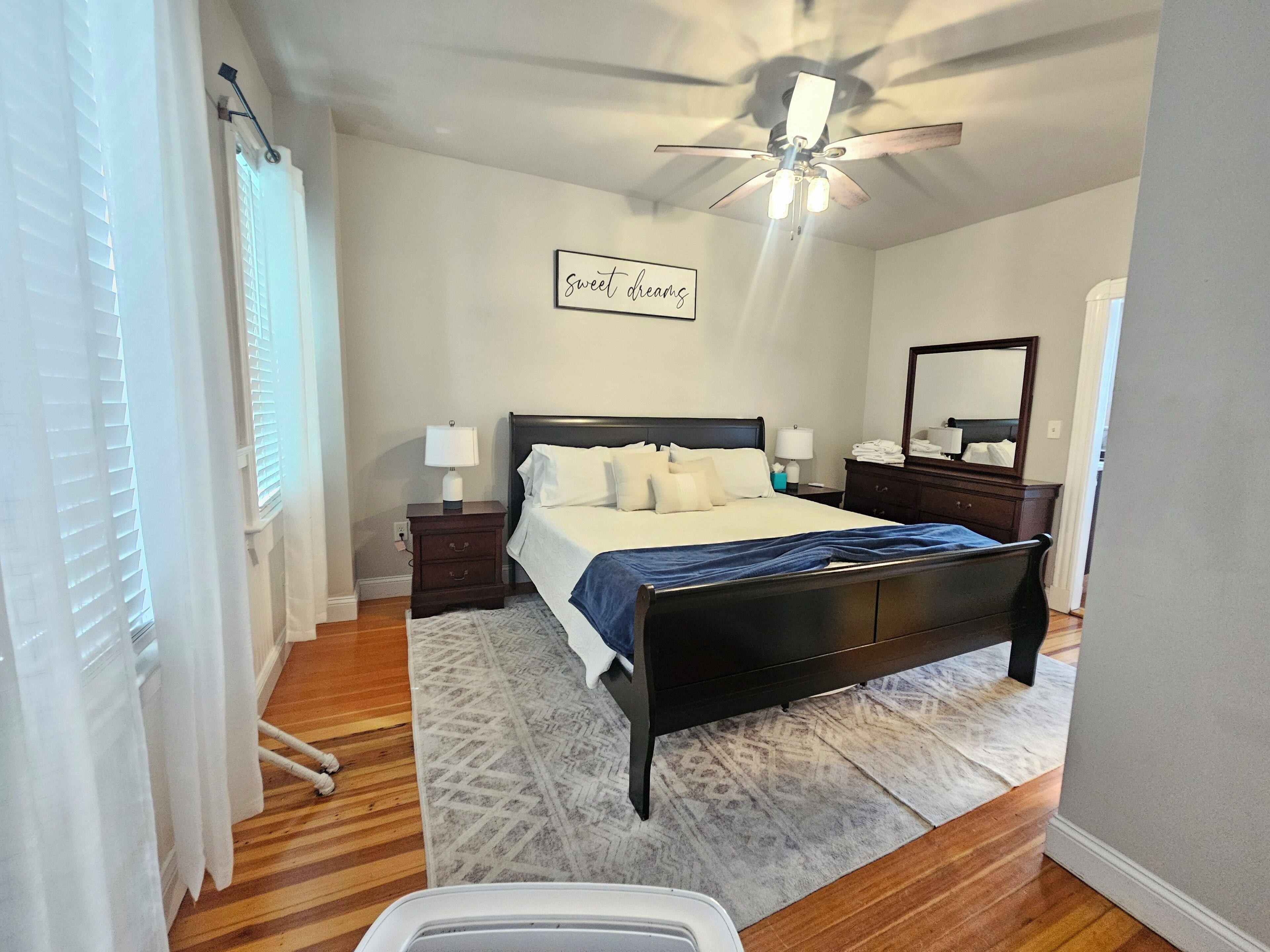 Une chambre à coucher comprenant un lit, des tables de chevet, un ventilateur de plafond, un miroir fixé au mur et un tapis.