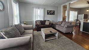 Ett rymligt vardagsrum med två soffor, ett soffbord och ett köksområde som syns genom en öppen dörröppning.