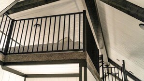 Un intérieur moderne avec un plafond haut, des poutres apparentes et un balcon doté d’une rambarde en métal.