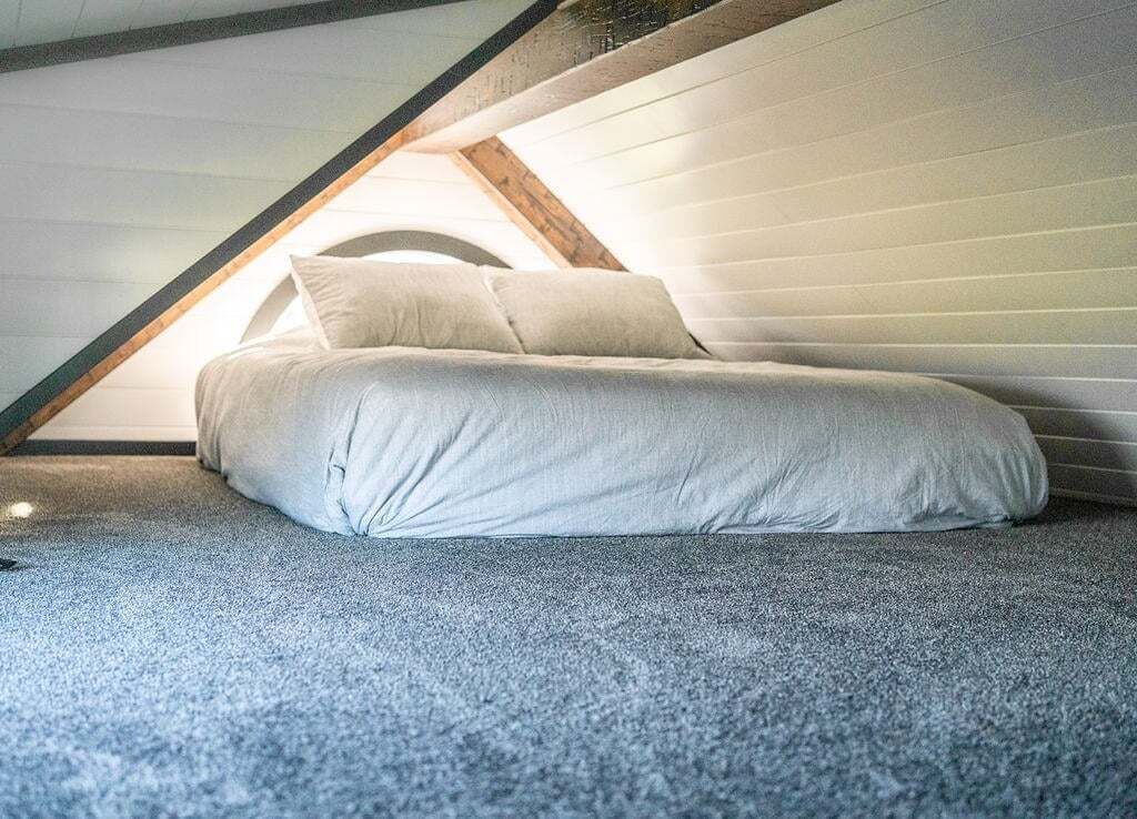 Un llit individual en una habitació d'estil loft amb sostre inclinat i vista al cel.