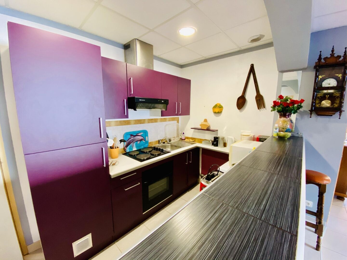 A modern kitchen with purple cabinets, a stainless steel range hood, and a wooden countertop.