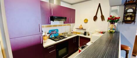 A modern kitchen with purple cabinets, a stainless steel range hood, and a wooden countertop.
