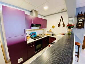 Eine moderne Küche mit violetten Schränken, einer Edelstahl-Dunstabzugshaube und einer Holzarbeitsplatte.