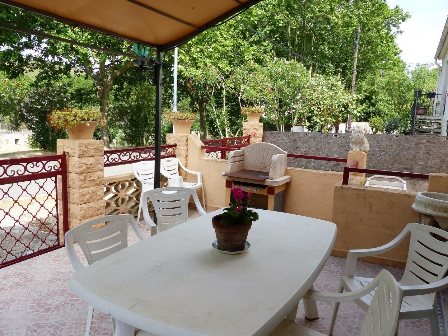 A covered patio with a table and chairs, a grill, and potted plants.
