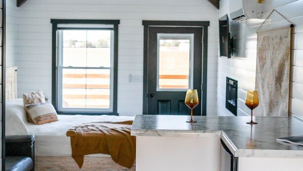 A modern kitchen with a marble countertop, a built-in oven, and a ceiling fan. - Whispering Cottage #3 | Shewana Tiny Home Village (Shipshewana)