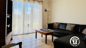 Una sala de estar con un sofá, una mesa de centro de madera y una araña. Hay un ventanal corredero que da a un balcón.