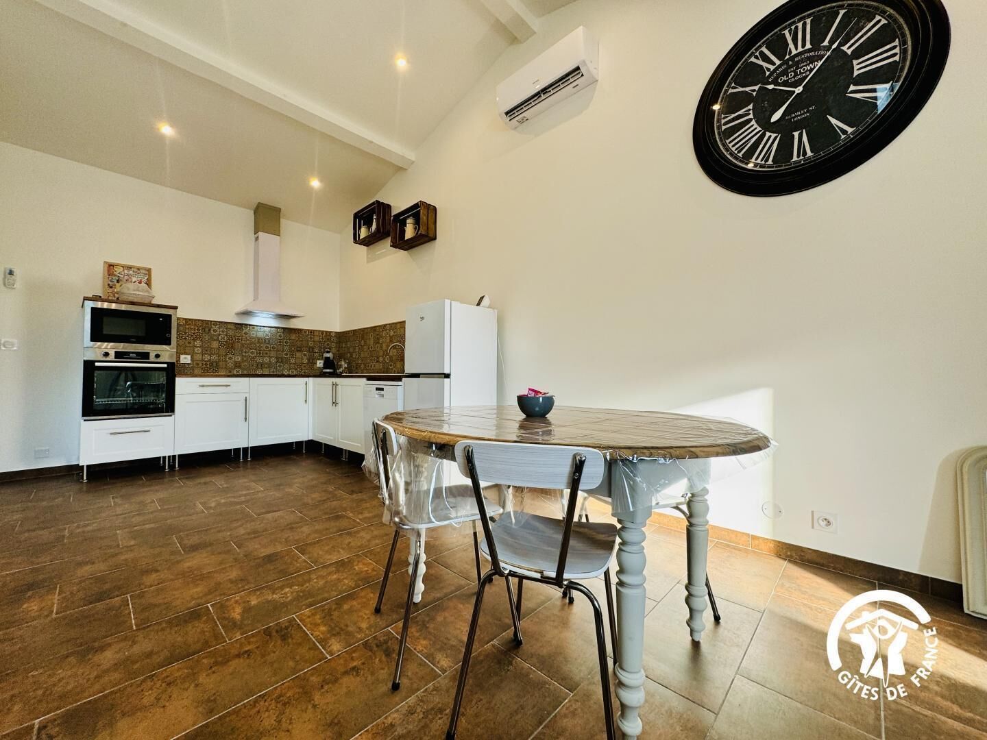 A modern kitchen with white cabinets, a built-in oven, and a large wall clock.