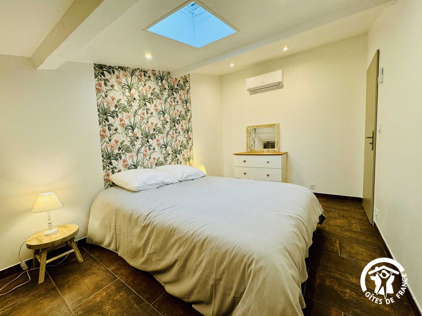 Een slaapkamer met een bed, nachtkastje, dressoir, dakraam en airconditioning.