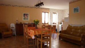 A dining area with a table, chairs, a sofa, a TV, and a kitchen in the background. - La Loggia - ROQUEFORT DES CORBIERES (ROQUEFORT DES CORBIERES)