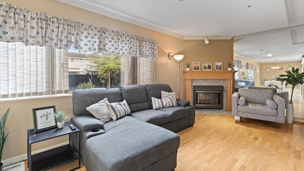 Ein Wohnzimmer mit einem grauen Ecksofa, einem kleinen Beistelltisch, einem Kamin und einem Essbereich im Hintergrund.
