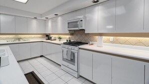 Eine moderne Küche mit weißen Schränken, einer eingebauten Mikrowelle, einem Gasherd und einer gefliesten Spritzschutzwand.
