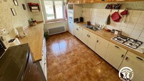 A kitchen with a gas stove, sink, and wooden cabinets. There is a window with a view of the outside. - La Grange - CAMURAC - Gîte (CAMURAC)