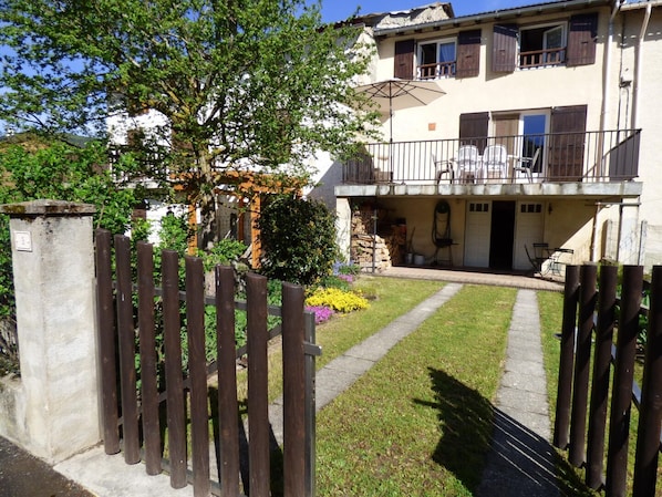 A two-story house with a balcony, a gated entrance, and a small garden with flowers.