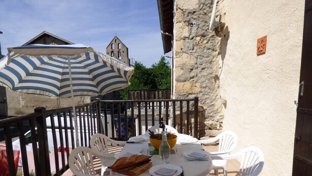 A terrace with white plastic chairs and a table set for dining, featuring a striped umbrella, a bottle, and a basket of bread. - La Grange - CAMURAC - Gîte (CAMURAC)
