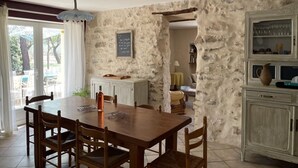 Un comedor con mesa y sillas de madera, una pizarra con escritura y una pared de piedra.