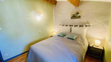 A bedroom with a bed, two pillows, a nightstand with a lamp, a wall-mounted picture, and a wooden ceiling beam.