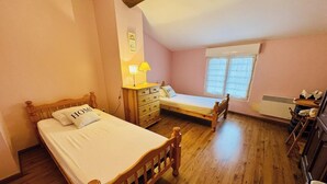 Une chambre à coucher avec un lit en bois, un plus petit lit, une commode, une lampe et une fenêtre.