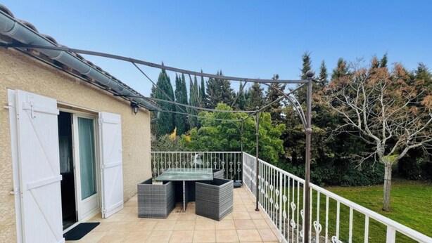 Un balcon avec une table et des chaises, une balustrade blanche et une vue sur des arbres et une pelouse.
