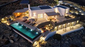 A modern house with a swimming pool, outdoor seating, and solar panels. - Heavenly views from Villa Nites with stunning infinity pool (Megas Gialos)
