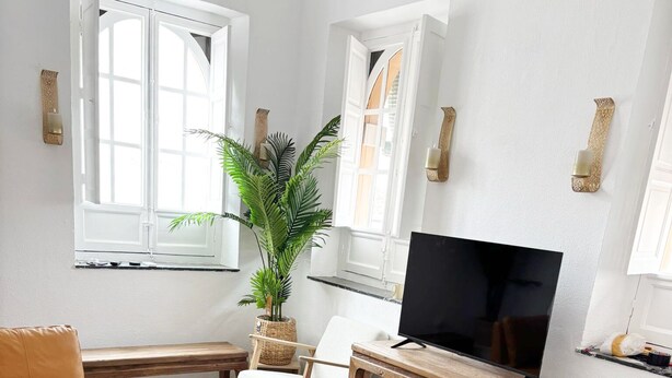 A living room with a sofa, chairs, a TV, a plant, and patterned flooring. - 2BR Cathedral & Giralda Views, Rooftop Terrace! (Sevilla)