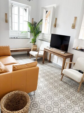 A living room with a sofa, chairs, a TV, a plant, and patterned flooring. - 2BR Cathedral & Giralda Views, Rooftop Terrace! (Sevilla)
