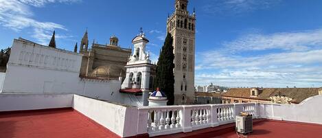 A rooftop terrace with a red floor, a white balustrade, and a view of a historic building with a tall tower.