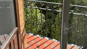 A balcony with a metal railing, a tiled floor, and a view of a building with a tiled roof and a white wall with a yellow trim. - 2BR Cathedral & Giralda Views, Rooftop Terrace! (Sevilla)