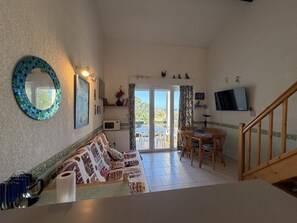 A cozy living room with a sofa, a dining table, and a TV. There's a staircase leading upstairs. - CYRNEA 27 - Walking distance to the beach - Air conditioning - Wi-Fi - Favone (CONCA)