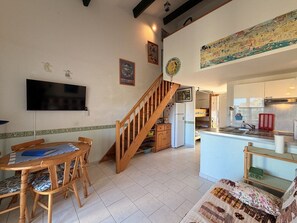 A spacious living area with a wooden staircase, a dining table with chairs, a kitchen area, and a television mounted on the wall. - CYRNEA 27 - Walking distance to the beach - Air conditioning - Wi-Fi - Favone (CONCA)
