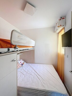 A small, clean room with a bunk bed, a desk, a chair, a TV, and a window with curtains. - Terrasse vue mer et montagne – Calvi centre et plage (CALVI)