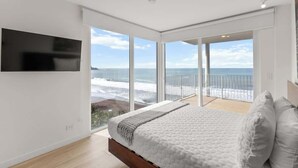 Un dormitorio con una cama grande, un televisor montado en la pared y un balcón con vista al océano.