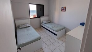 Ein kleiner, sauberer Raum mit zwei Einzelbetten, einem Deckenventilator, einem Fenster mit Meerblick und einem kleinen Schreibtisch.