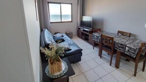 Ein Wohnzimmer mit einer Couch, einem Esstisch mit Stühlen, einem Fernseher und Blick aufs Meer.