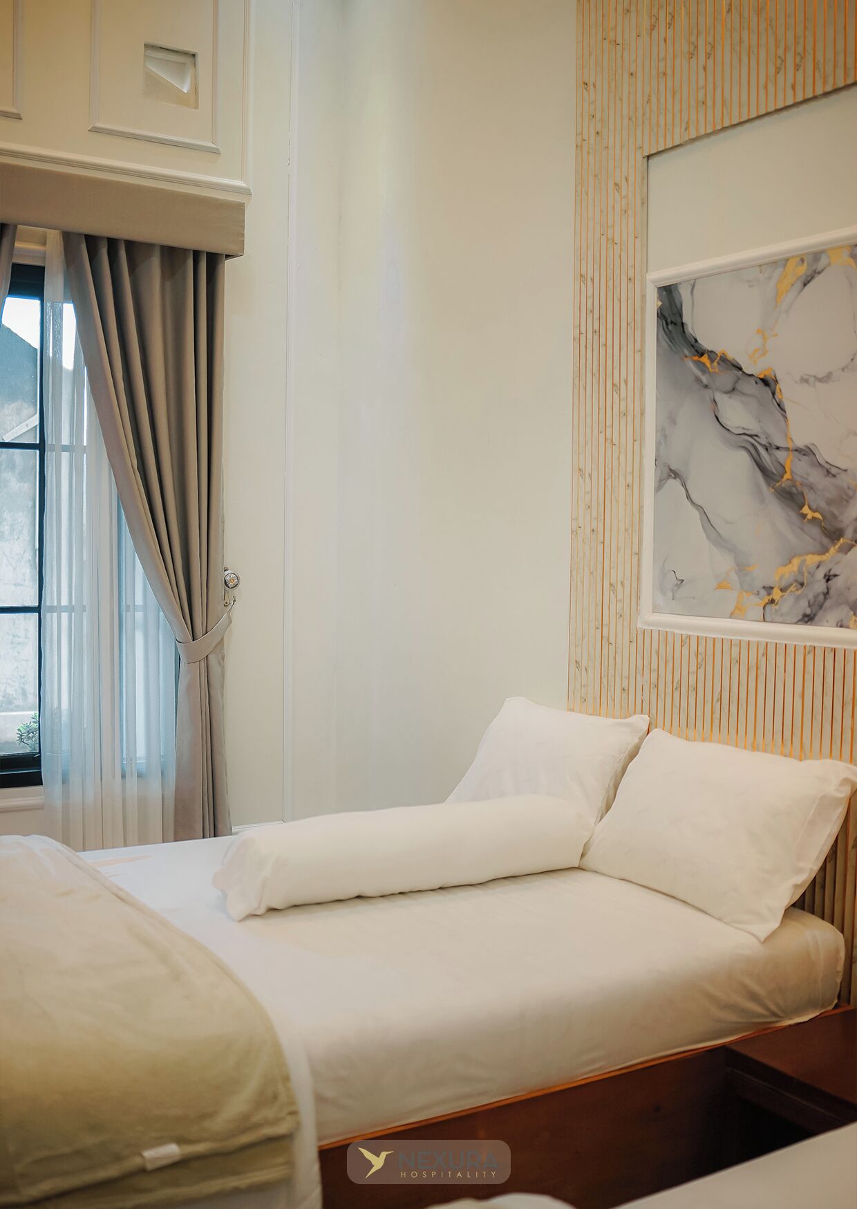 Une chambre d’hôtel avec un lit, une fenêtre avec des rideaux, un mur recouvert de panneaux en bois et une œuvre d’art en marbre.