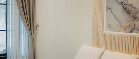 Une chambre d’hôtel avec un lit, une fenêtre avec des rideaux, un mur recouvert de panneaux en bois et une œuvre d’art en marbre.