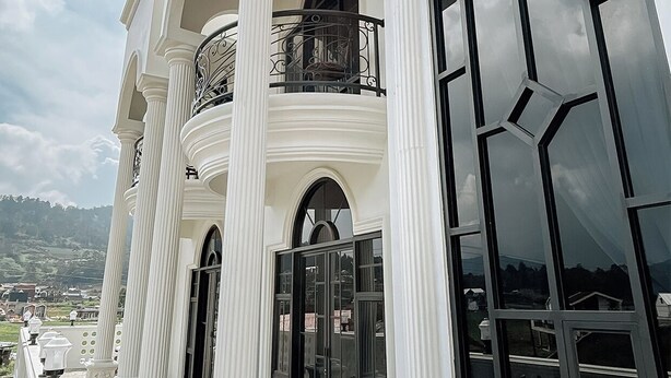 Un imposant bâtiment aux colonnes blanches, doté de grandes fenêtres en arc de cercle et d’un balcon orné de balustrades travaillées.