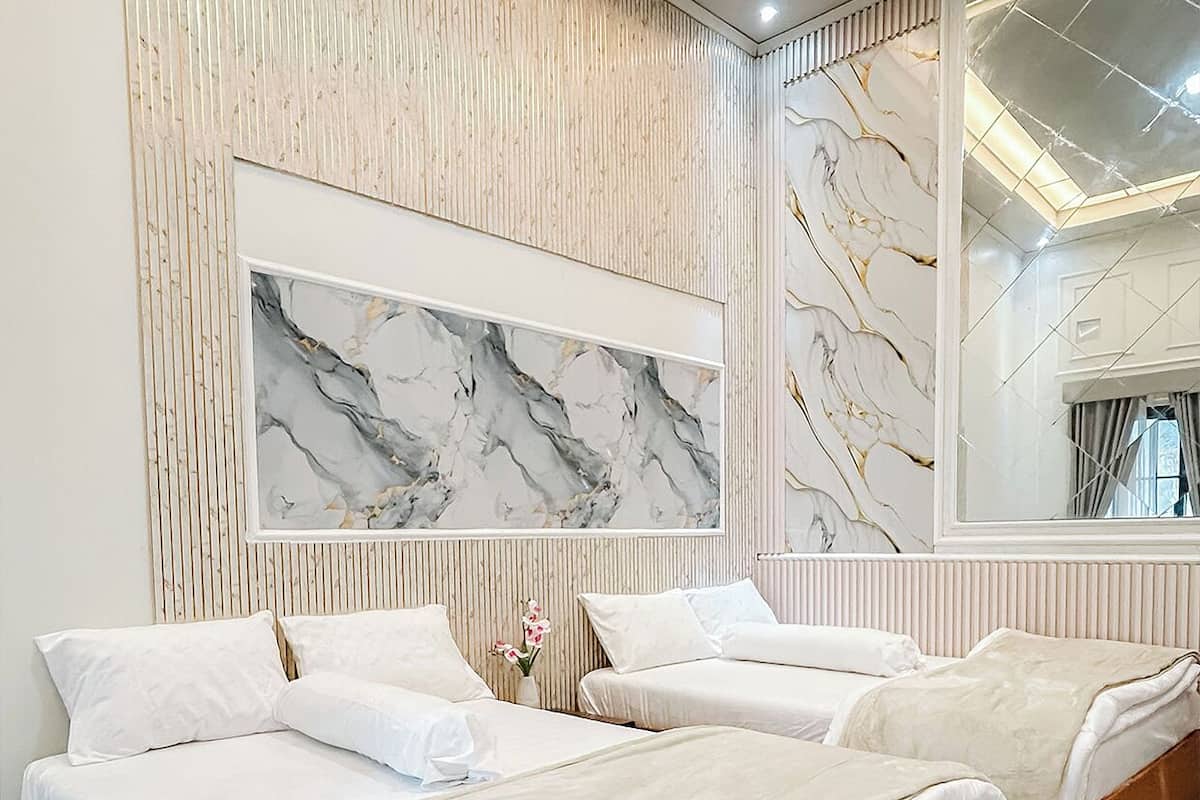 A hotel room with three beds, a marble wall, and a large mirror.